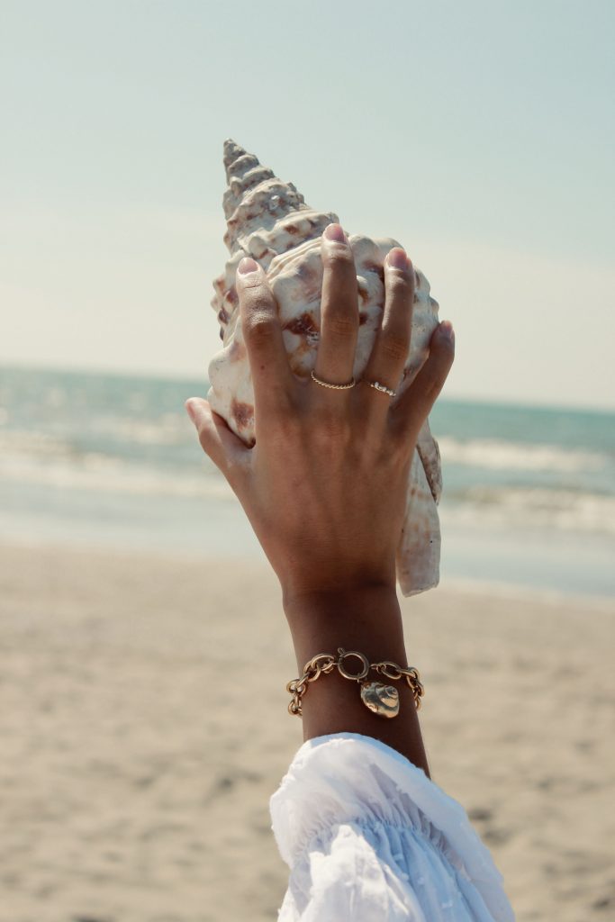 Girl at te beach holding a sea shell horn wearing gold jewellery l A la collection jewellery